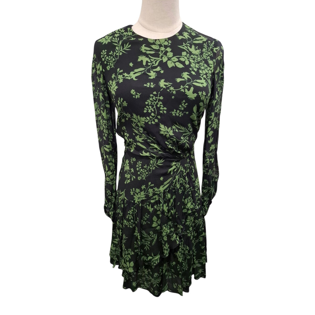 A long-sleeve wrap-style dress with a green botanical leaf pattern on a black background, displayed on a mannequin torso against a plain white background.