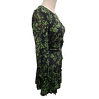 A black long-sleeve wrap dress with an all-over green floral pattern, displayed on a mannequin torso against a plain white background.