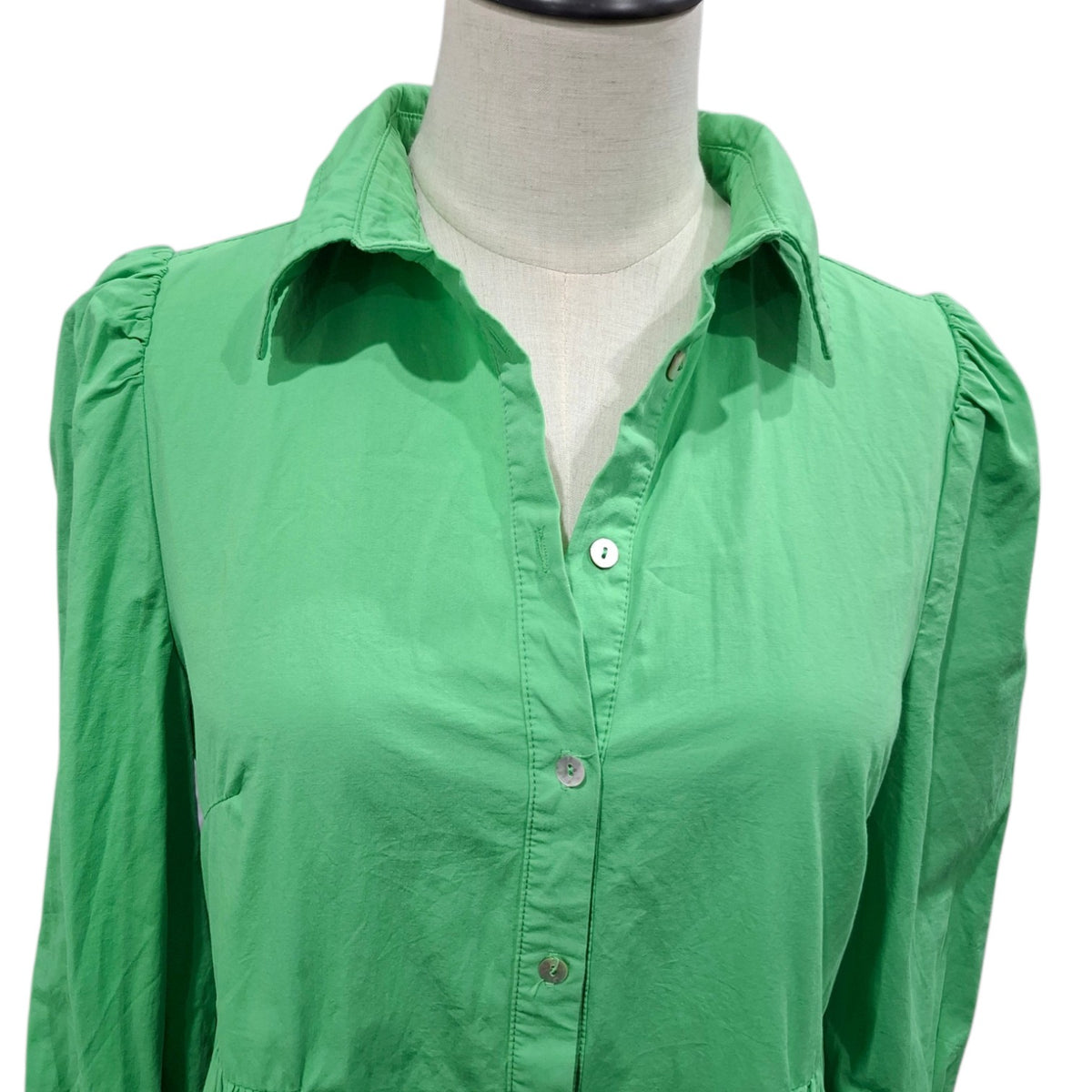 A bright green long-sleeve button-up blouse with puffed shoulders and a pointed collar, displayed on a cream-colored dress form against a white background.