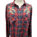 A red and navy plaid button-up shirt with green and yellow stripe details, featuring embroidered red and pink flowers with green leaves on both shoulders, displayed on a cream dress form against a white background.