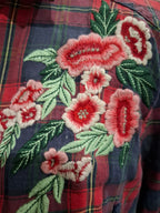 Close-up of a red and navy plaid shirt with detailed floral embroidery featuring pink and red flowers and green leaves.