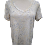 A short-sleeve V-neck top on a dress form, featuring a textured, abstract pattern in beige and muted gray-blue tones.