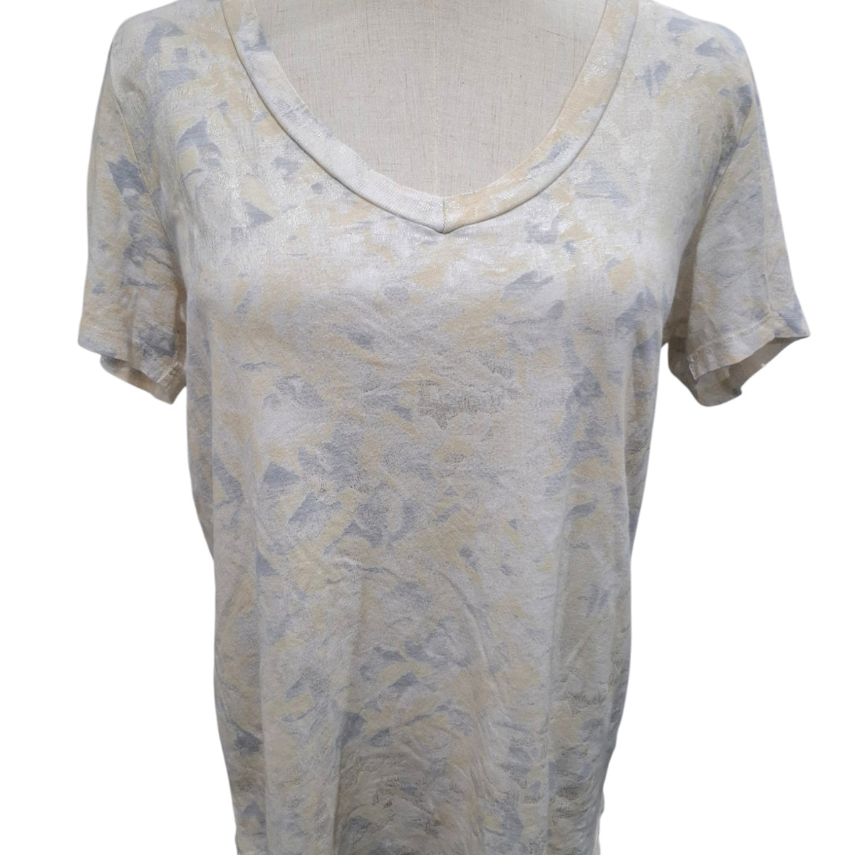 A short-sleeve V-neck top on a dress form, featuring a textured, abstract pattern in beige and muted gray-blue tones.