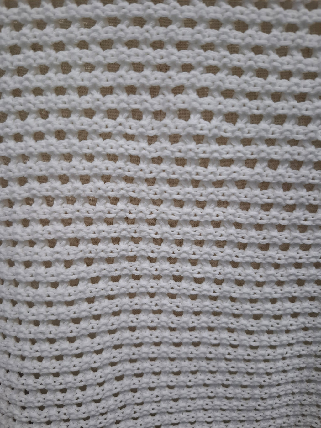 A close-up of a white crocheted fabric with a textured openwork pattern, filling the entire frame.
