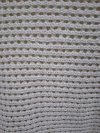 A close-up of a white crocheted fabric with a textured openwork pattern, filling the entire frame.