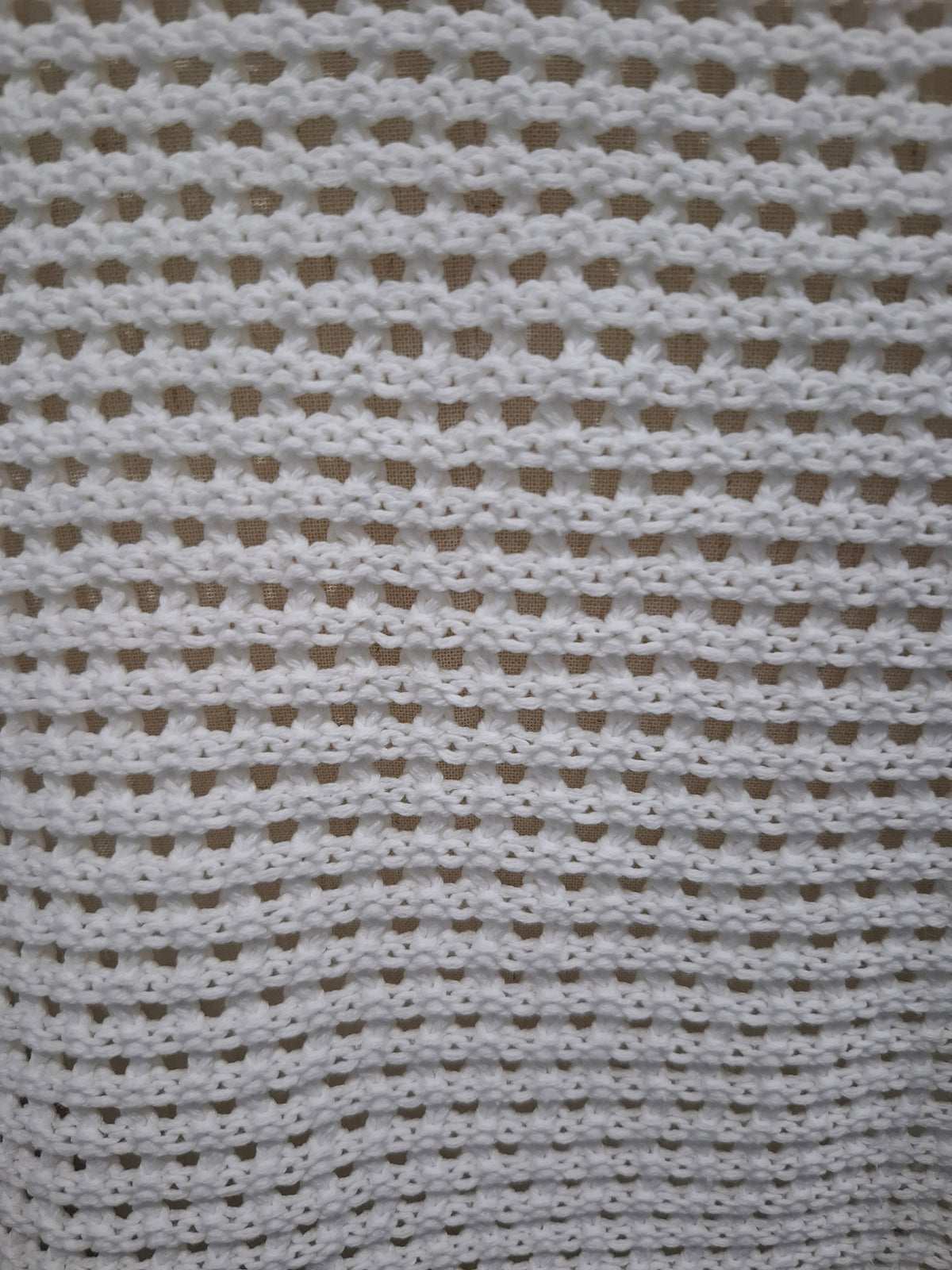 A close-up of a white crocheted fabric with a textured openwork pattern, filling the entire frame.