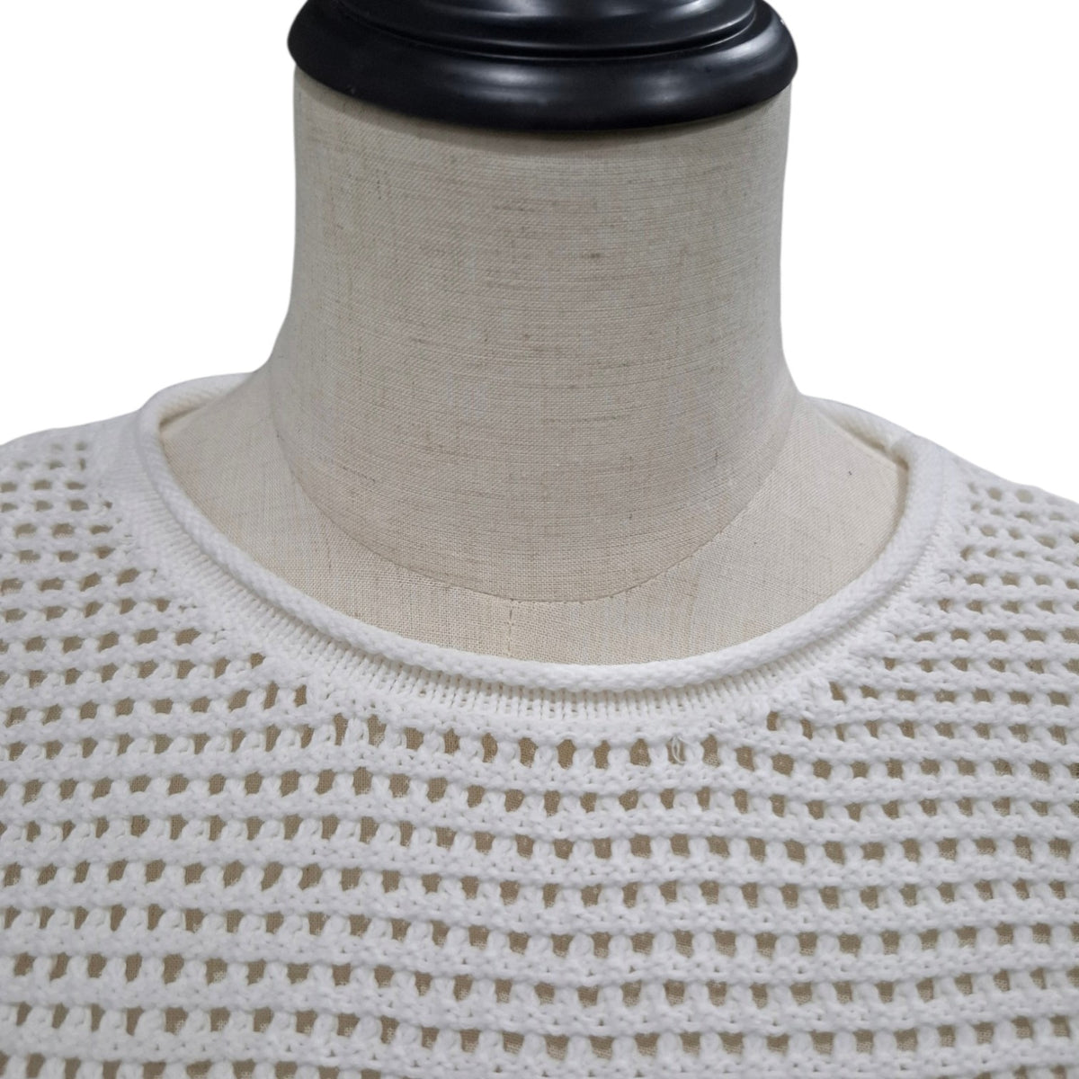 Close-up of a cream-colored open-knit sweater displayed on a beige fabric mannequin torso against a white background.