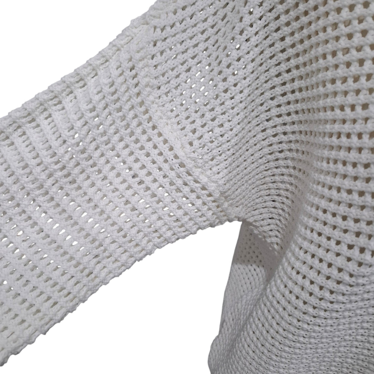 Close-up of a white open-knit sweater fabric, showing the textured knit pattern and sleeve construction against a plain white background.
