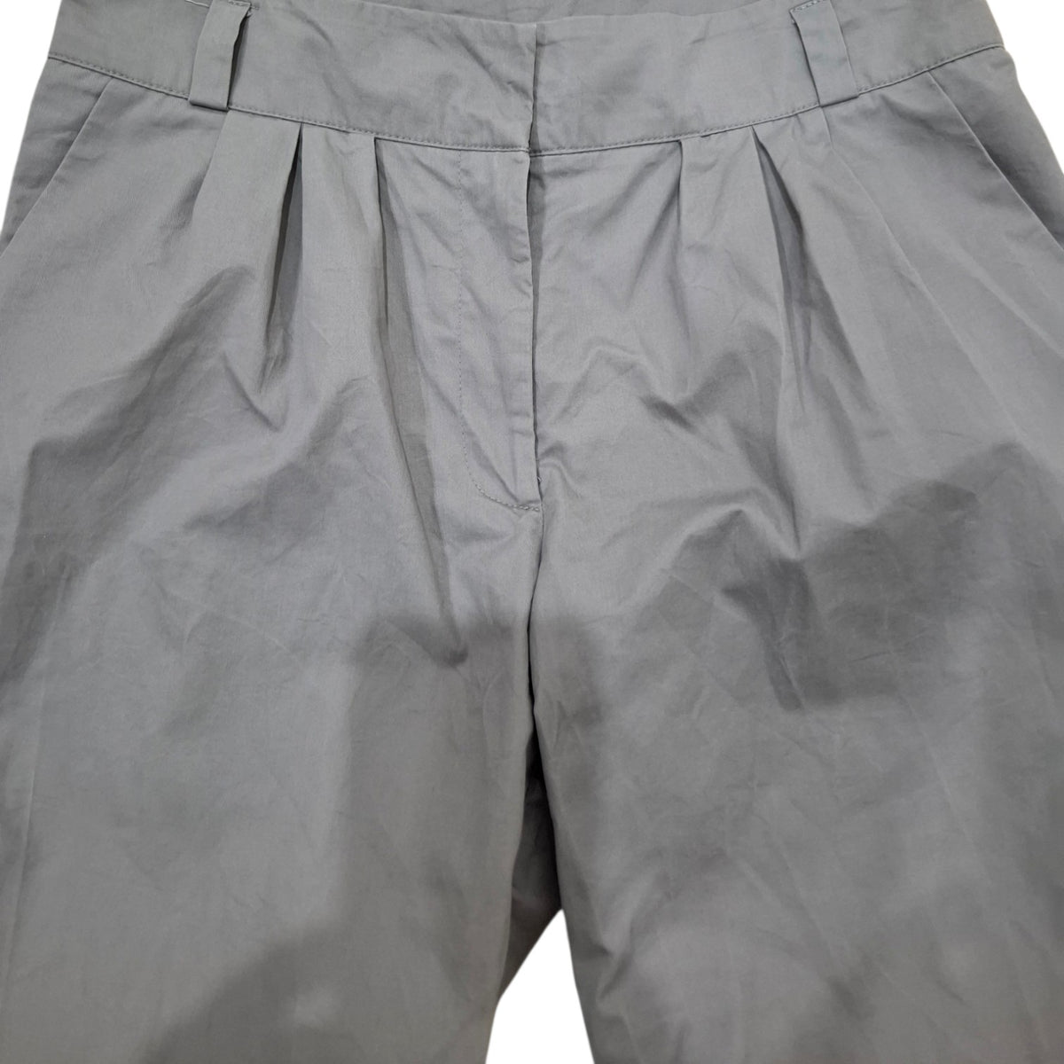 Close-up of gray pleated trousers showing the waistband, front center seam, and fabric texture.