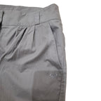 Close-up of gray pleated shorts with a small white embroidered Quiksilver logo on the lower leg, set against a plain white background.