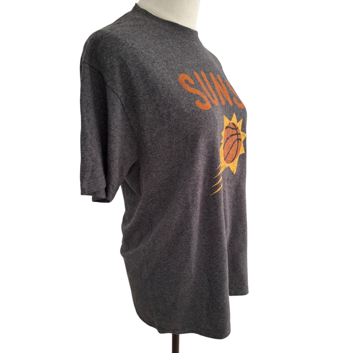 A dark heather gray short-sleeve t-shirt displayed on a mannequin torso, featuring a distressed orange and yellow Phoenix Suns graphic on the front.