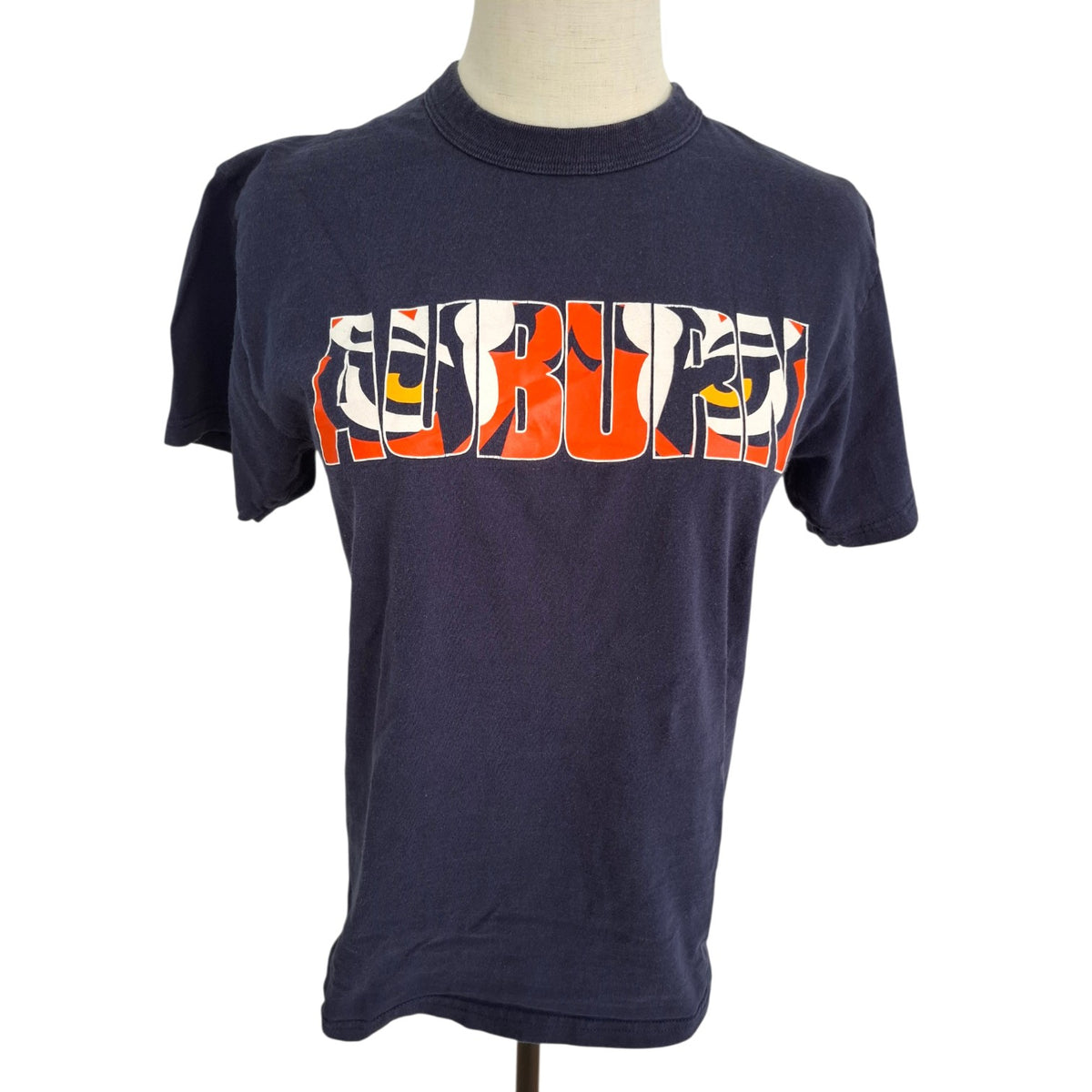 A navy blue short-sleeve t-shirt displayed on a mannequin torso against a white background. The shirt features a large graphic across the chest spelling 'REBORN' in orange, white, and black stylized lettering with yellow details.