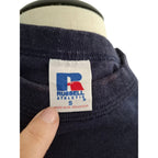 Close-up of a navy blue Russell Athletic sweatshirt on a mannequin, showing the neck label and a finger pointing at it.