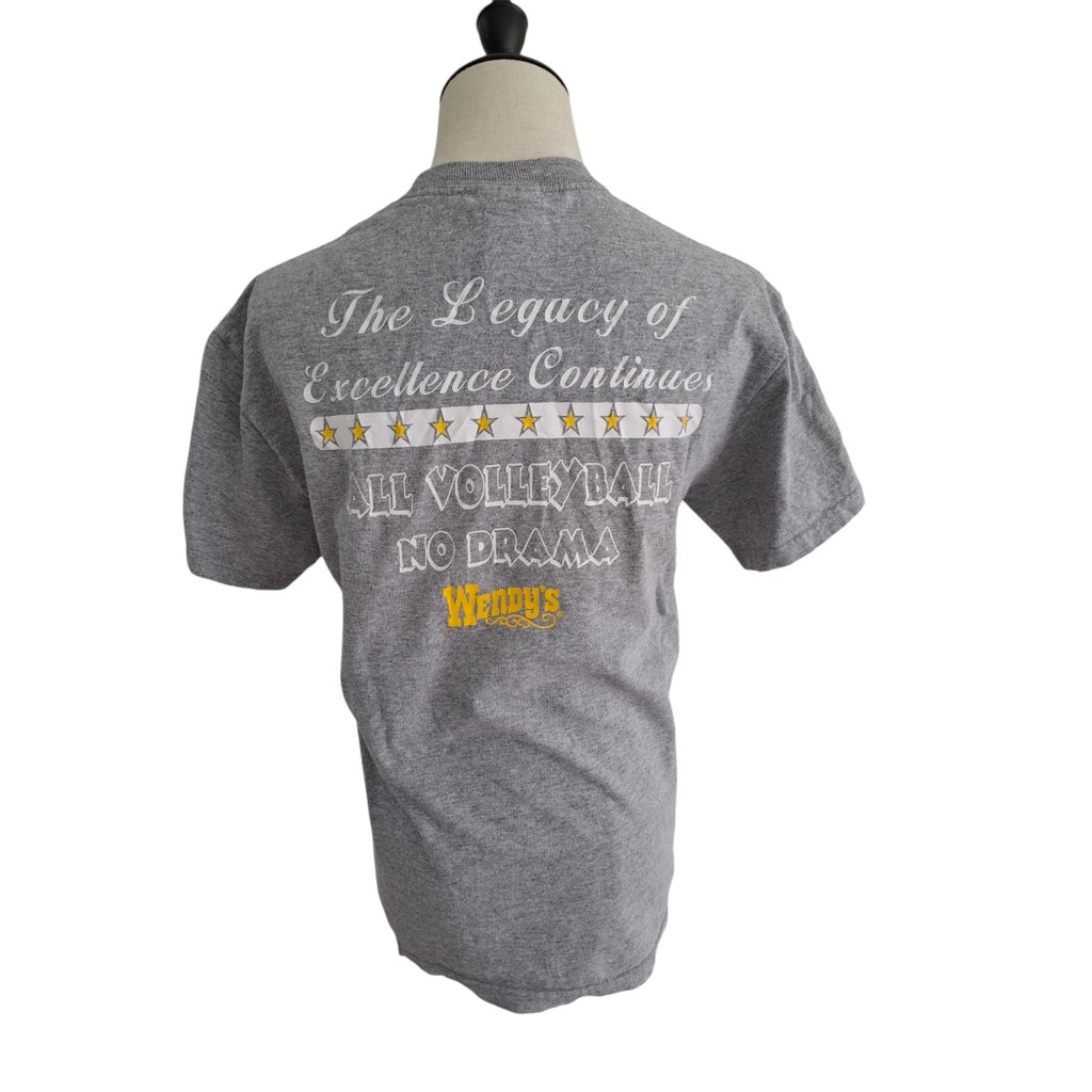 A heather gray short-sleeve t-shirt displayed on a mannequin torso, showing the back graphic with the text 'The Legacy of Excellence Continues', a row of gold stars, 'ALL VOTERS BATE NO DRAMA', and 'Wrigley's' in yellow.