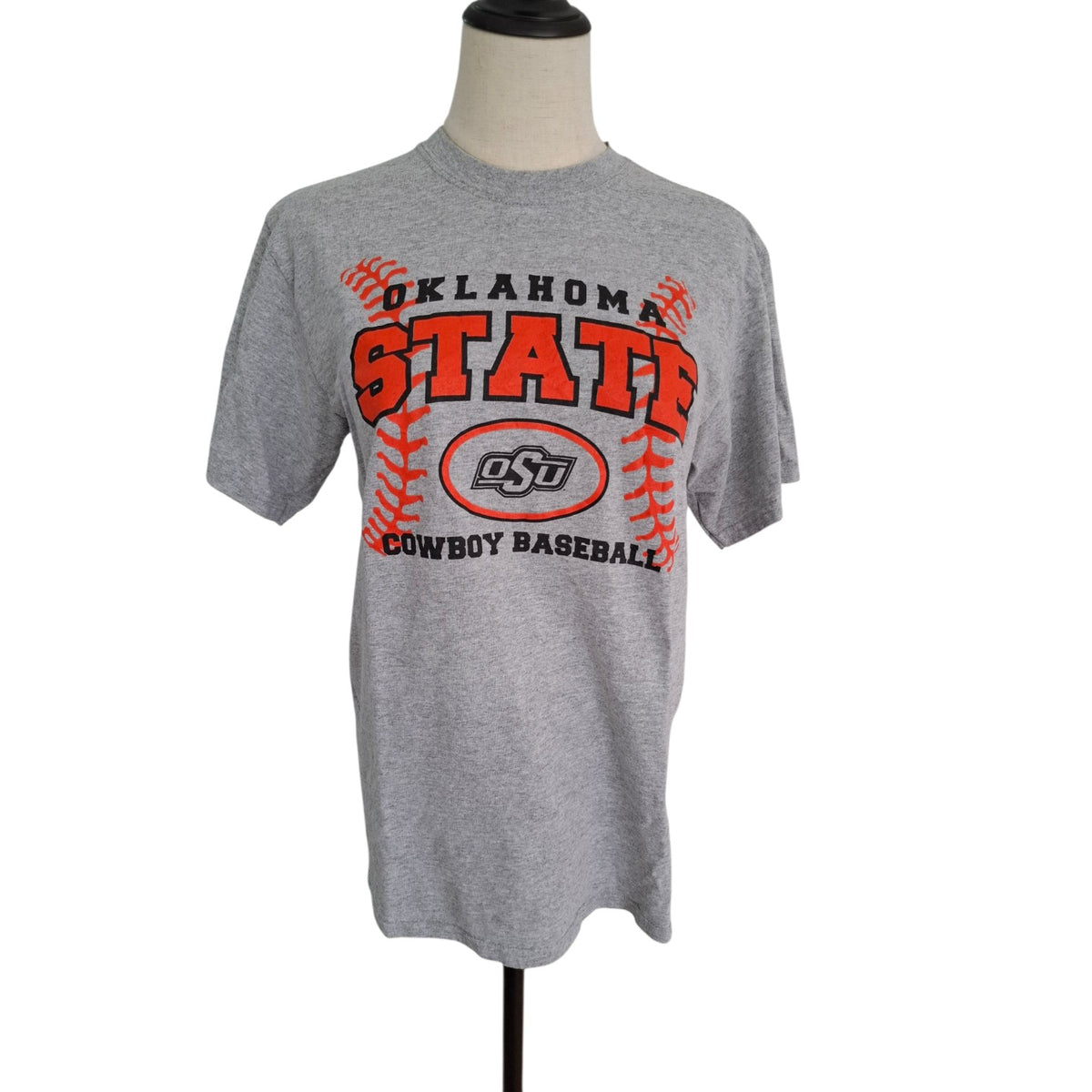 A heather gray short-sleeve t-shirt displayed on a mannequin torso against a white background. The shirt features a graphic with 'OKLAHOMA STATE' in red and black, a baseball design, and the 'OSU' logo in the center, with 'COWBOY BASEBALL' printed below.