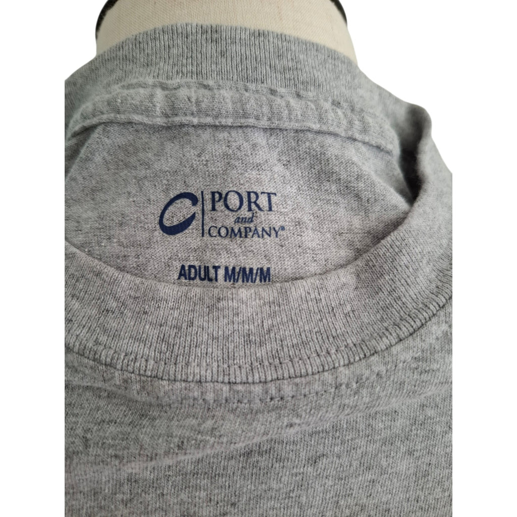 Close-up of a gray heather crewneck t-shirt on a mannequin, showing the inner neck label with the navy blue 'PORT and COMPANY' logo and 'ADULT M/M' text.