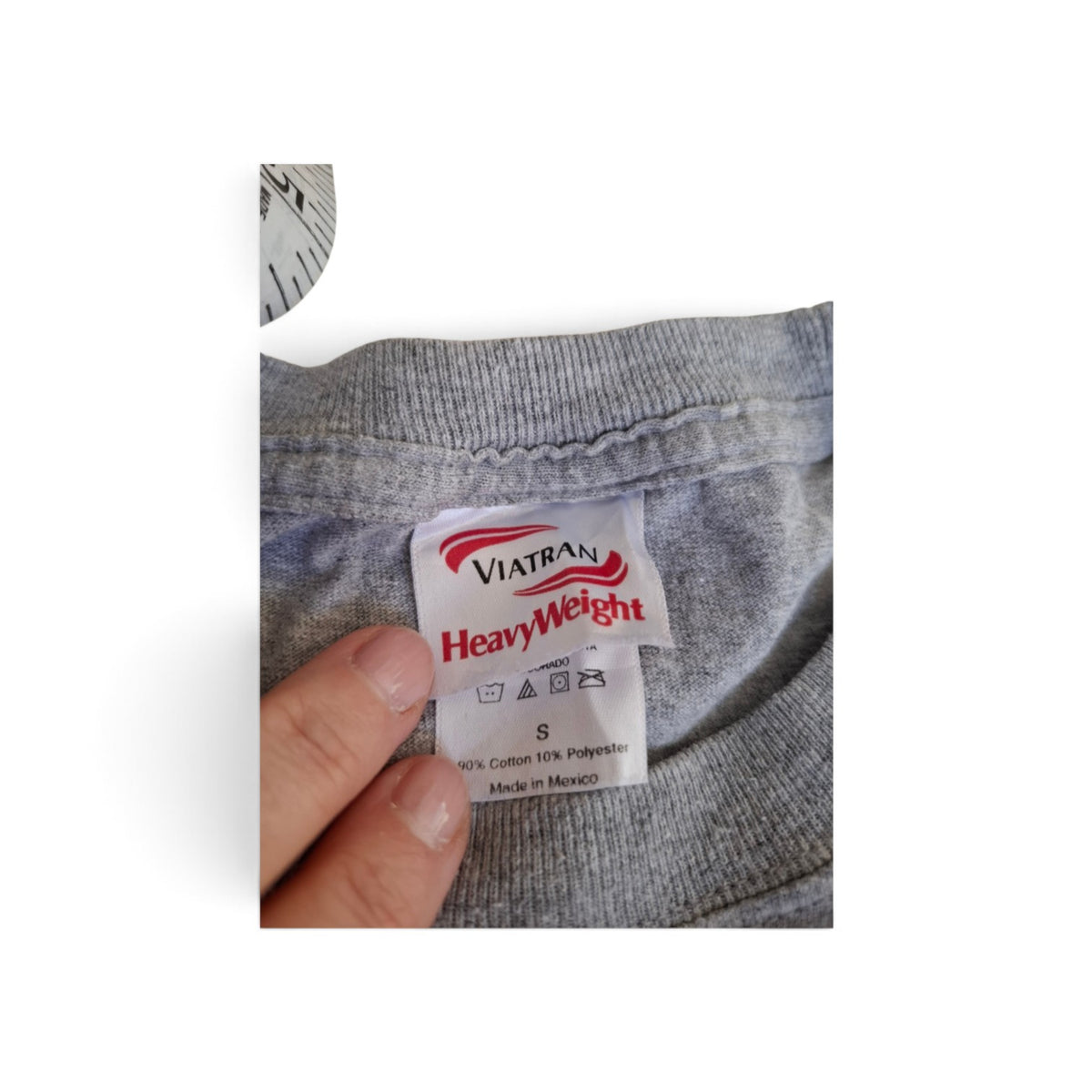 Close-up of a gray knit garment neck label reading VIATRAN HeavyWeight, with a finger holding the label in place against a white background.