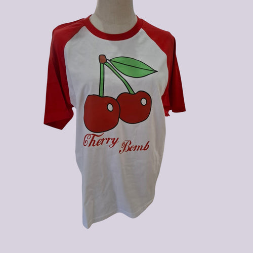 A white and red raglan t-shirt displayed on a mannequin torso, featuring a graphic of two red cherries with green leaves and the text 'Cherry Bomb' printed below.