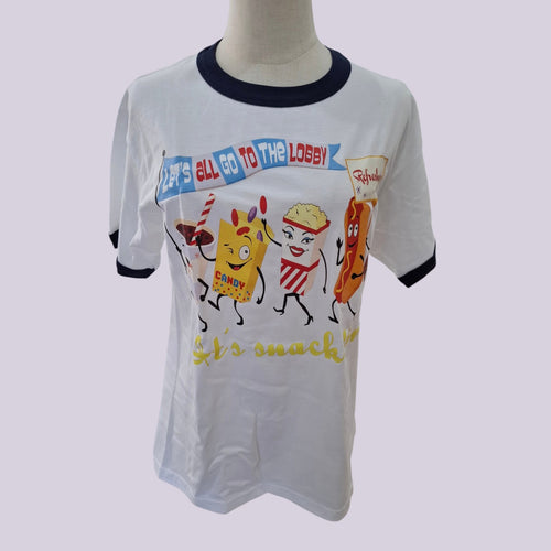 A white ringer t-shirt with dark navy blue collar and sleeve trim, featuring a colorful cartoon graphic of snack characters and the text 'LET'S ALL GO TO THE LOBBY' and 'Let's snack!'.