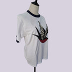 White ringer t-shirt with a navy blue crew neck and sleeve cuffs, featuring a large printed swallow graphic on the front with black, white, and red details, displayed on a mannequin torso.