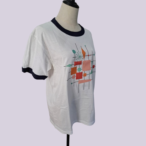 A white ringer t-shirt with black trim on the collar and sleeve cuffs, featuring a colorful abstract geometric print on the front, displayed on a mannequin torso against a light lavender background.