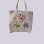 An off-white canvas tote bag with two shoulder straps, featuring a retro mid-century modern floral pattern with pink, yellow, and purple starburst shapes on a light lavender background.