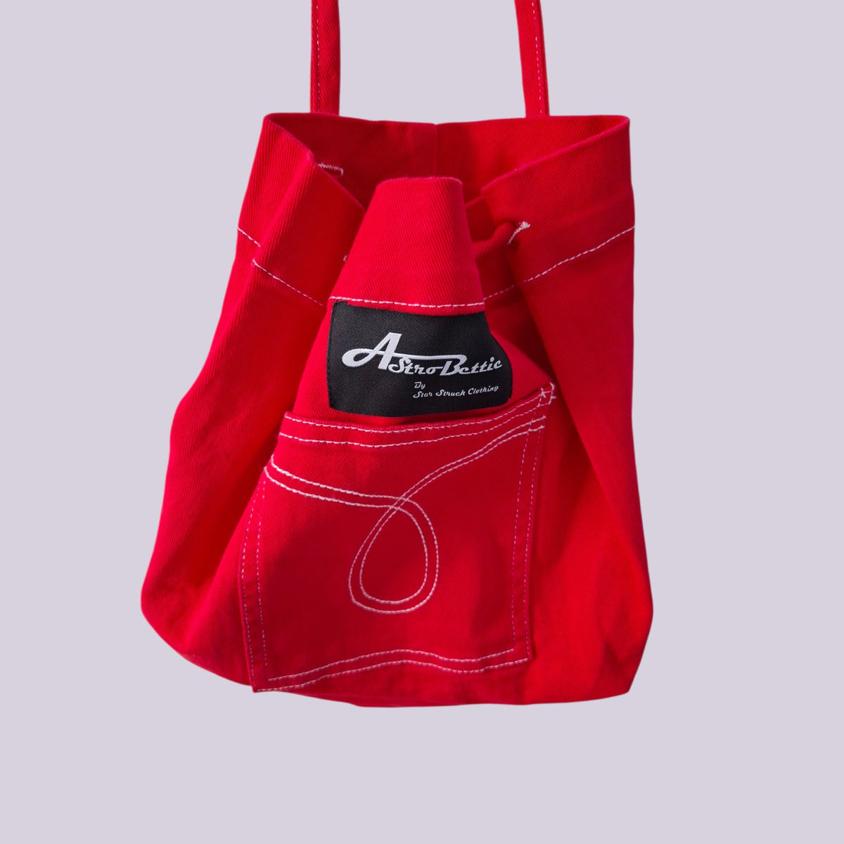 A bright red canvas tote bag with white contrast stitching, featuring a front pocket with a black brand label that reads 'A Breeze Bottle San Francisco, California'.