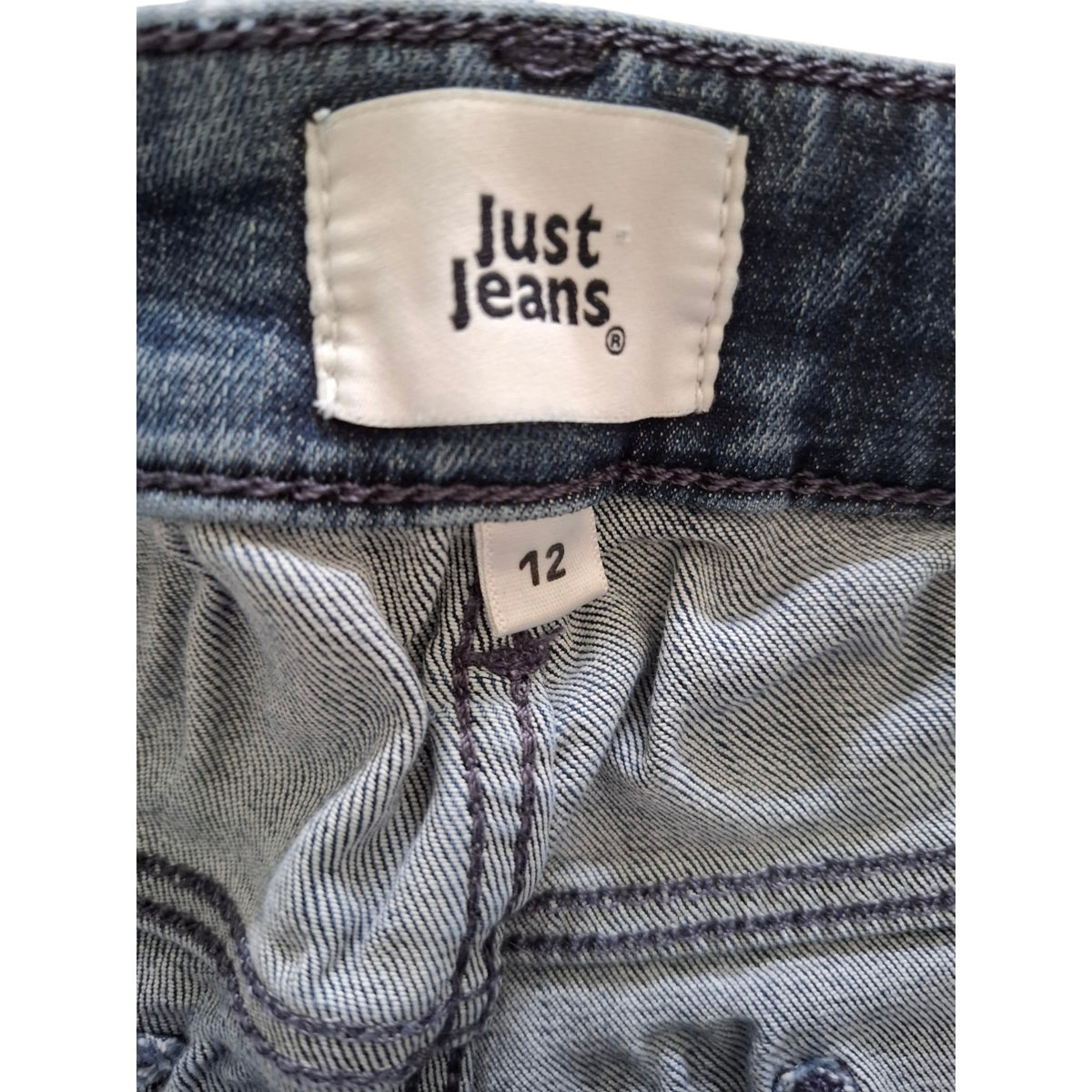 Close-up of the waistband of a pair of blue denim jeans, showing the white 'Just Jeans' brand label and a size '12' tag.