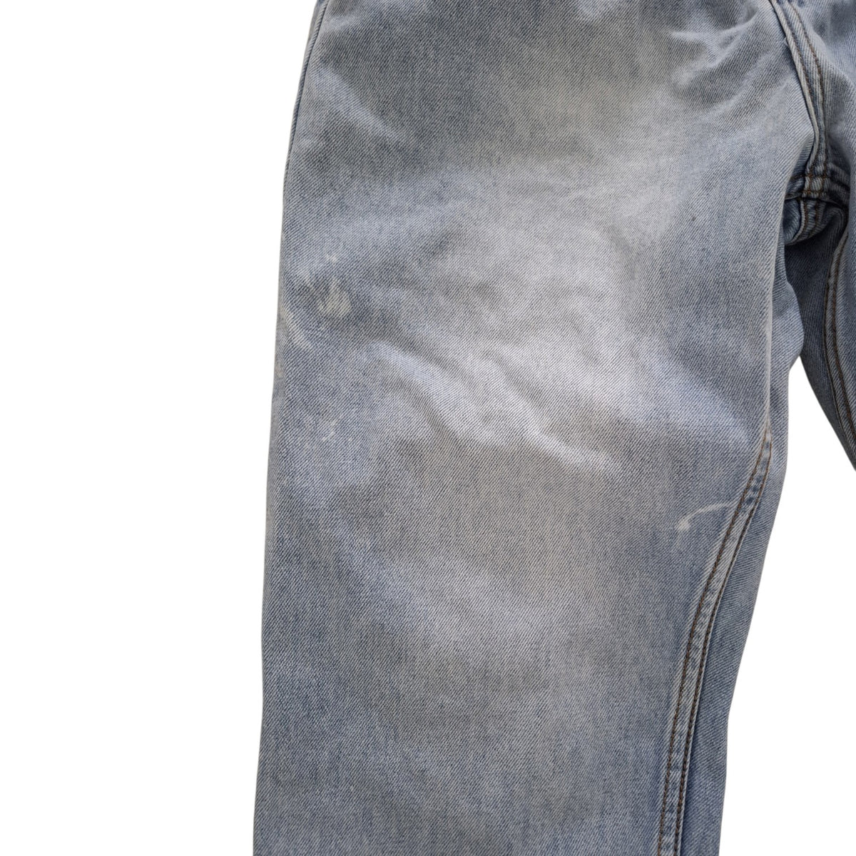 Close-up of a light blue denim garment, showing the fabric texture, fading, and a seam on a plain white background.