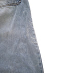 Close-up of a light blue denim fabric, showing the texture and a portion of a pocket seam against a plain white background.