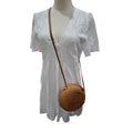 A white short-sleeve eyelet dress displayed on a mannequin, styled with a round woven brown crossbody bag against a plain white background.