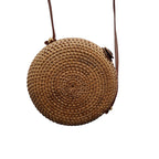 A round woven straw crossbody bag with a brown leather strap, shown against a plain white background.