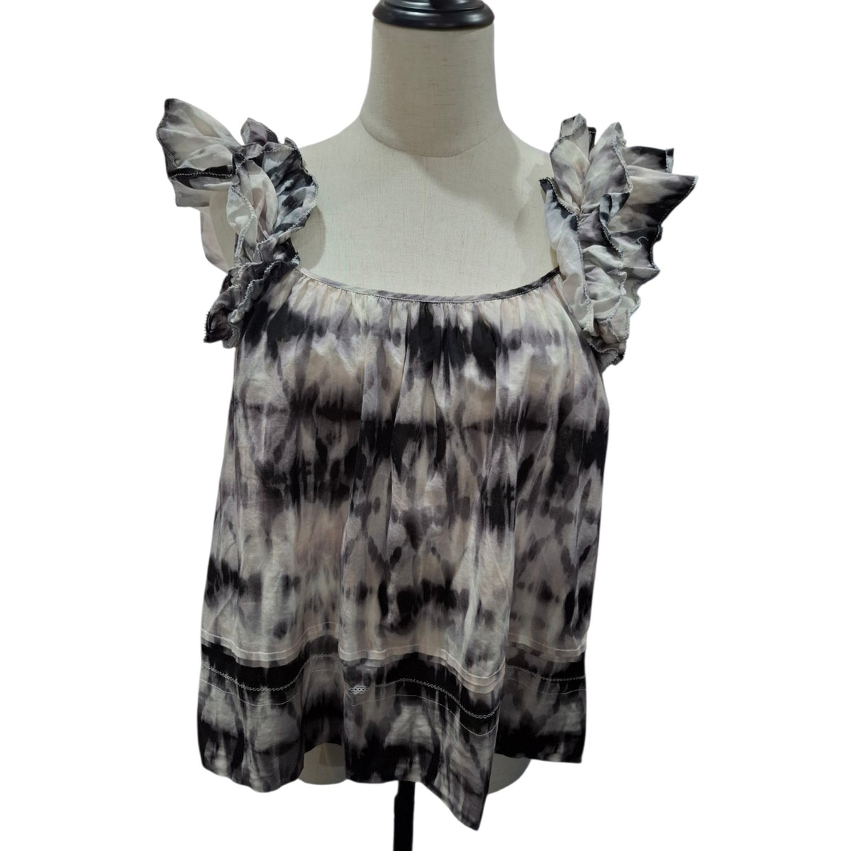 A women's sleeveless top with ruffled shoulder straps, displayed on a cream-colored dress form mannequin. The top features a black, gray, and beige tie-dye pattern.