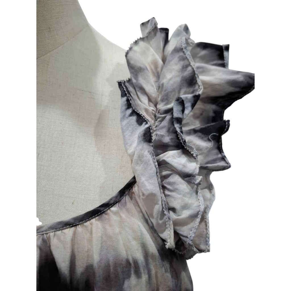 Close-up of a ruffled top on a mannequin torso, featuring layered ruffles in a gray and black tie-dye pattern against a white background.