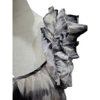 Close-up of a ruffled top on a mannequin torso, featuring layered ruffles in a gray and black tie-dye pattern against a white background.