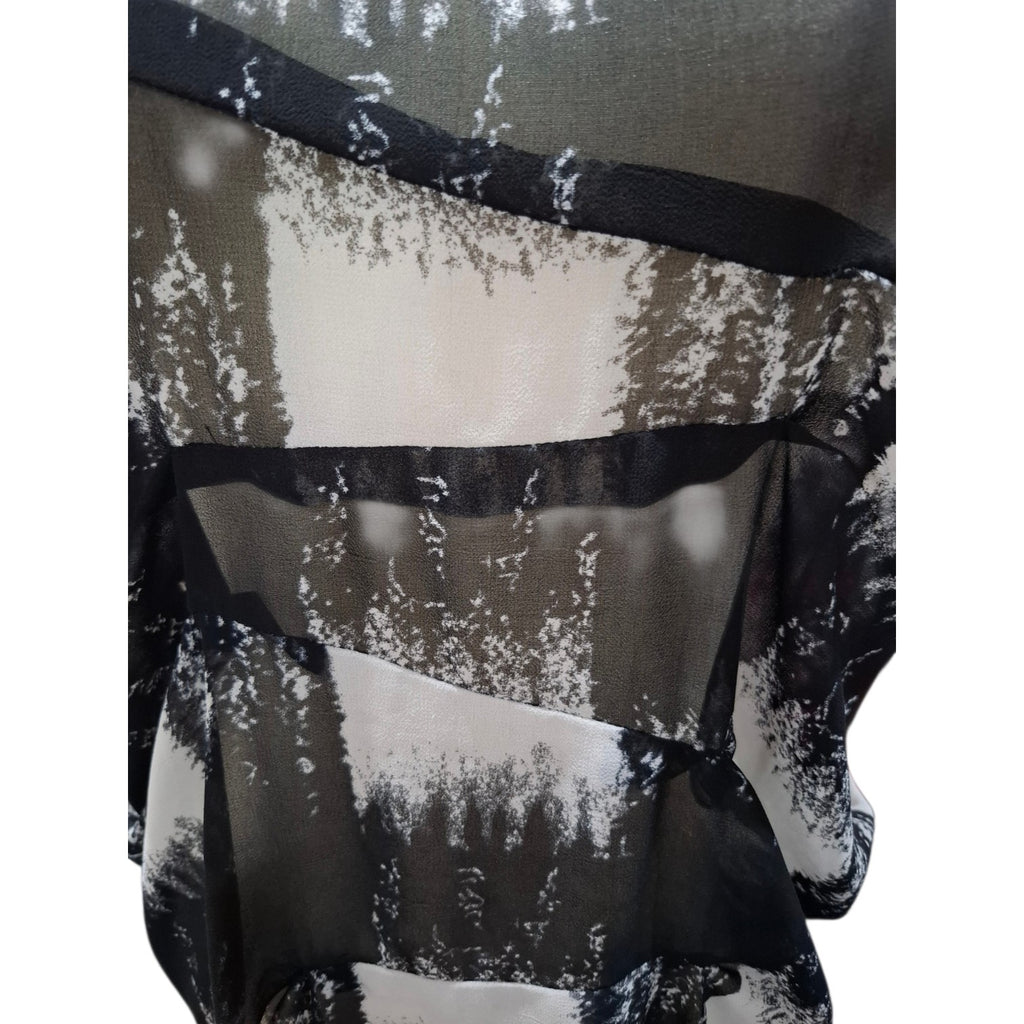 A close-up of a sheer black and white abstract patterned fabric, likely a scarf or shawl, with layered ruffles and black trim.