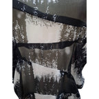 A close-up of a sheer black and white abstract patterned fabric, likely a scarf or shawl, with layered ruffles and black trim.