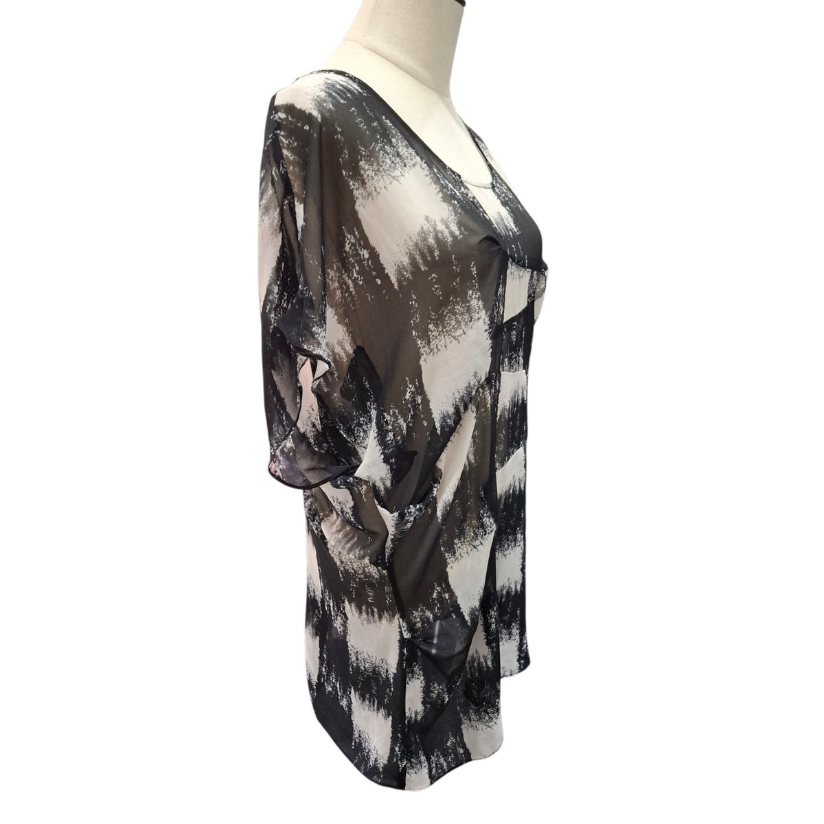 A sheer black and beige abstract print tunic top displayed on a mannequin torso against a white background.