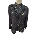 A black lace long-sleeve blouse with a high mock neck and ruffled chest detail, displayed on a mannequin torso against a white background.