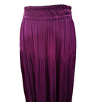 A close-up of a pleated skirt in a rich magenta-purple color, featuring an elastic waistband and tiered construction, shown against a plain white background.