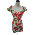 A white short dress with a red and green floral print, featuring puff sleeves and a sweetheart neckline, displayed on a mannequin torso against a white background.