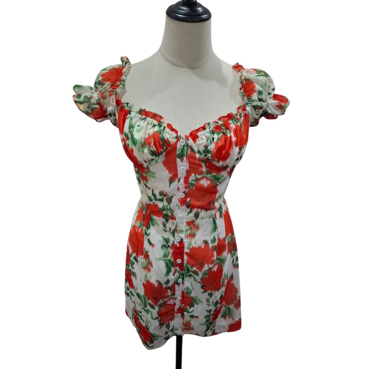 A white short dress with a red and green floral print, featuring puff sleeves and a sweetheart neckline, displayed on a mannequin torso against a white background.