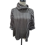 A black and white houndstooth patterned blouse with a high draped mock neck and elbow-length sleeves, displayed on a mannequin torso against a white background.