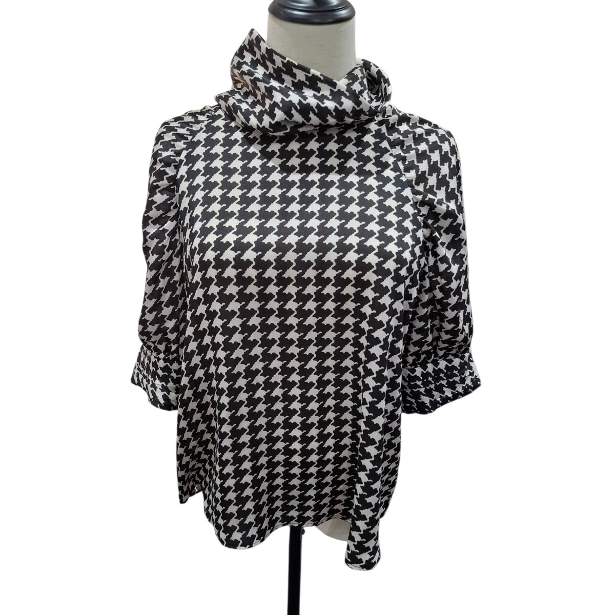 A black and white houndstooth patterned blouse with a high draped mock neck and elbow-length sleeves, displayed on a mannequin torso against a white background.