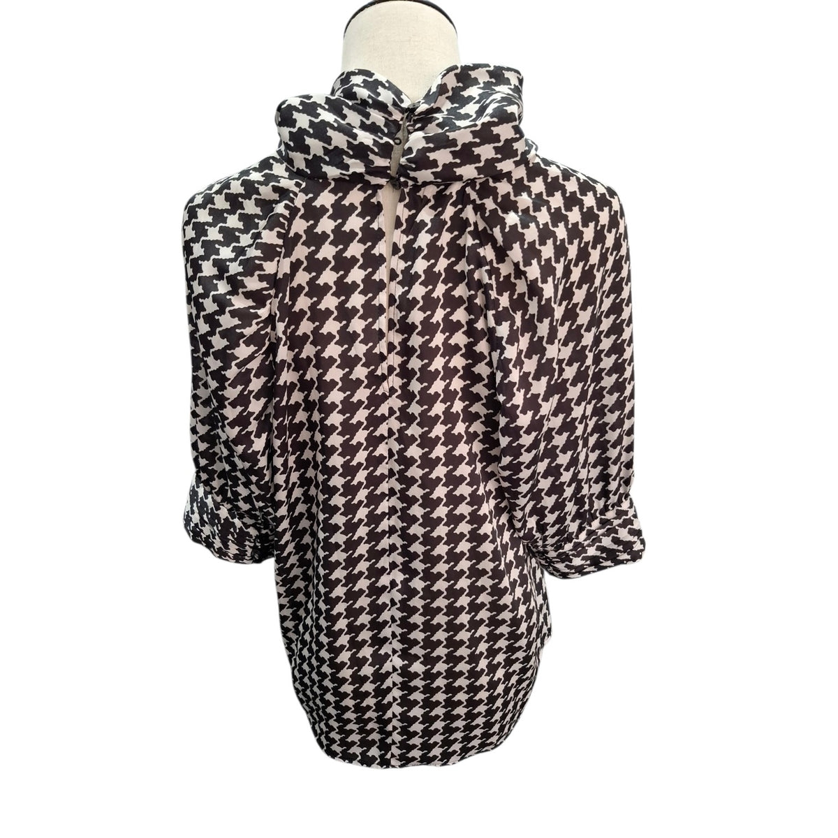 A black and beige houndstooth patterned blouse with a high gathered collar and three-quarter sleeves, displayed on a mannequin torso against a white background.