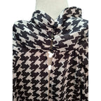 A black and off-white houndstooth patterned blouse displayed on a mannequin torso, featuring a high collar and a central button placket.