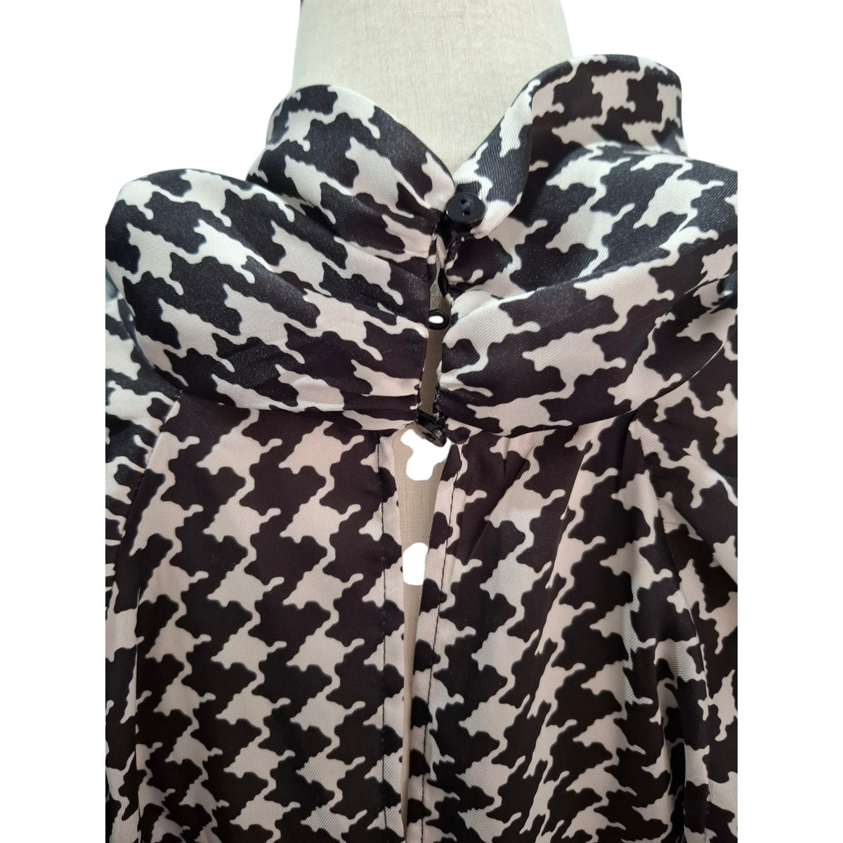 A black and off-white houndstooth patterned blouse displayed on a mannequin torso, featuring a high collar and a central button placket.
