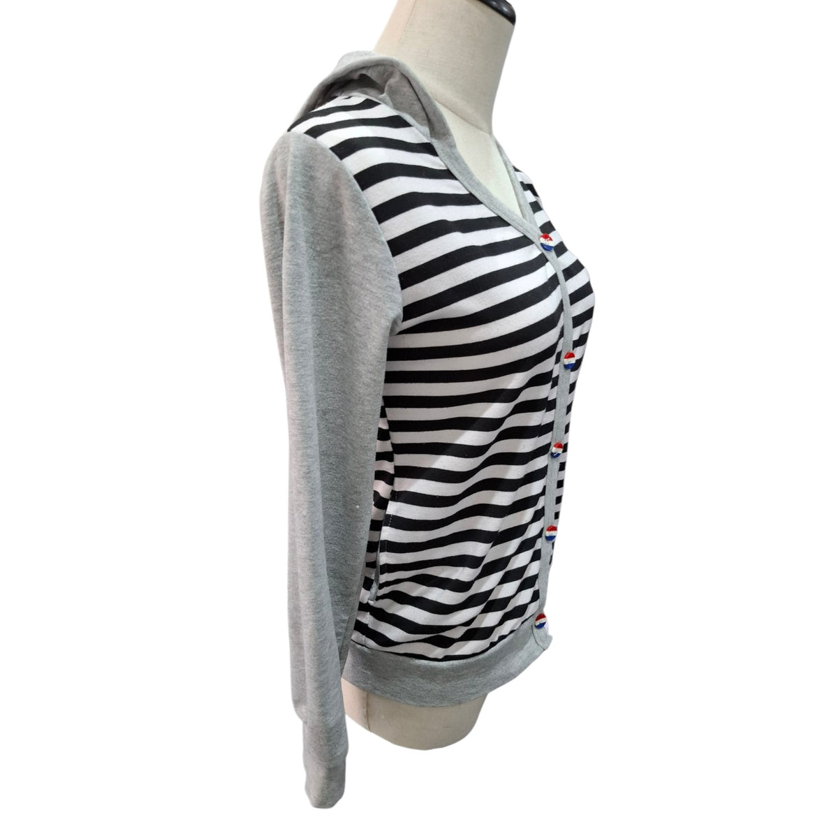 A women's long-sleeve hooded top displayed on a mannequin torso against a plain white background. The garment has a black and white striped body with a solid light gray hood and sleeves, and small red and blue embroidered accents near the placket.