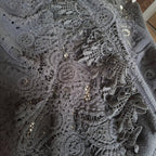 Close-up of a dark gray lace fabric with intricate floral patterns and small metallic sequins.