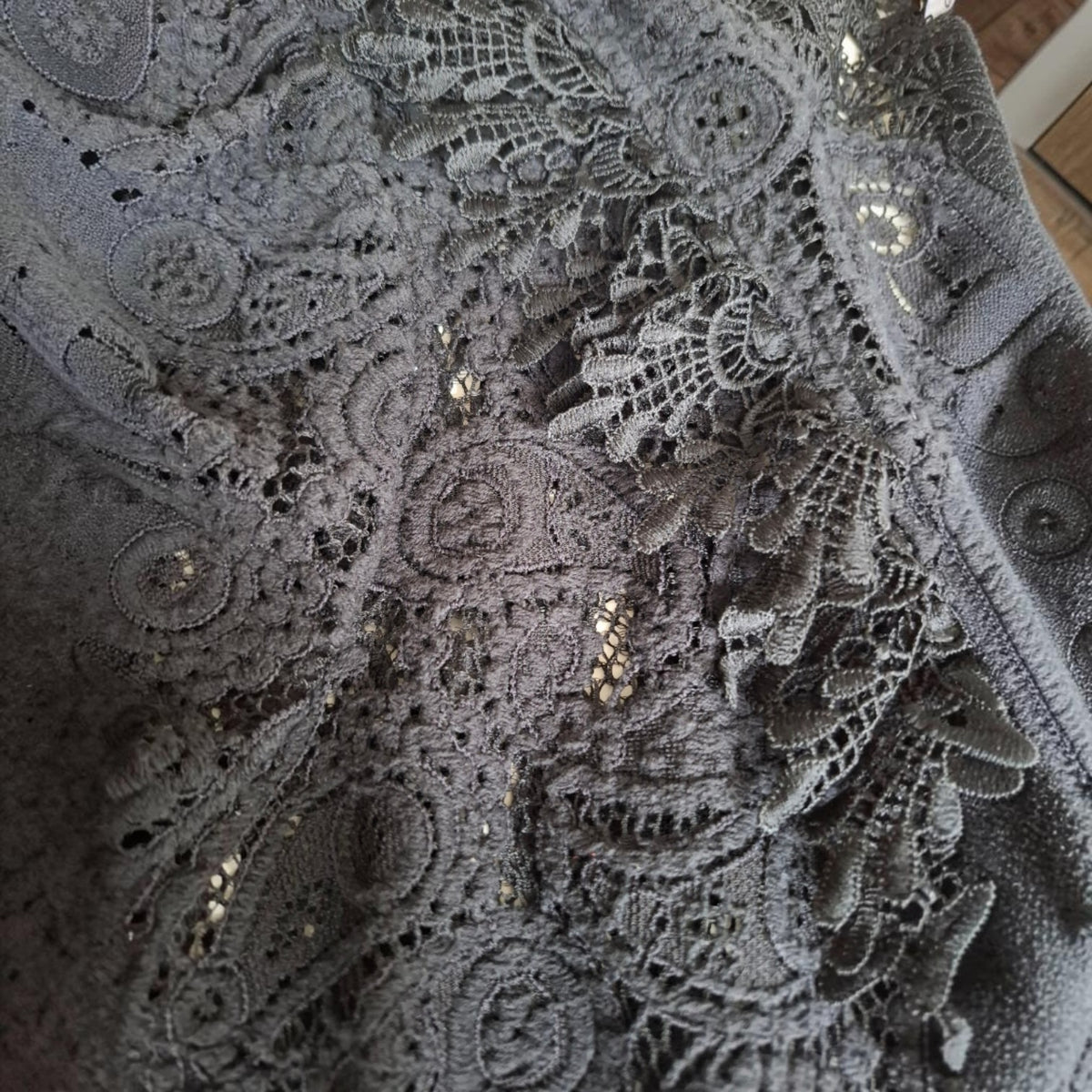 Close-up of a dark gray lace fabric with intricate floral patterns and small metallic sequins.